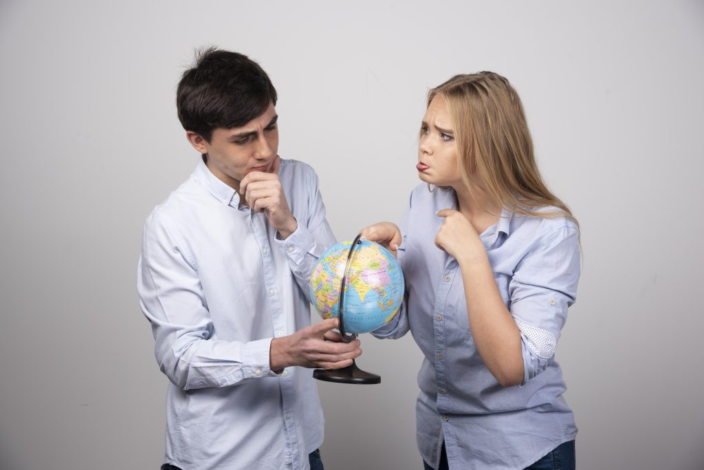 jeune couple debout devant un globe terrestre sur un mur gris
